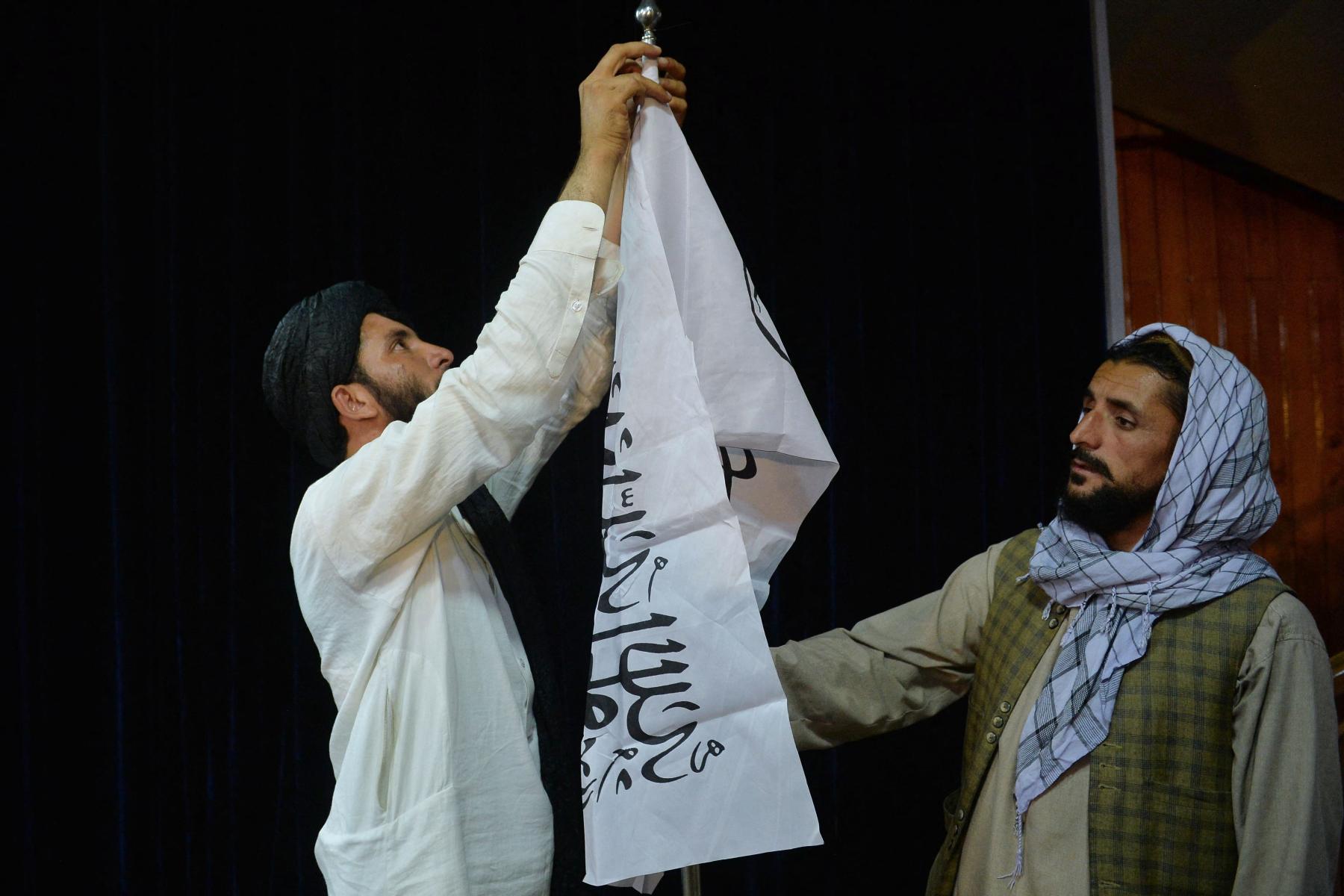 Men adjust the Taliban flag before the arrival of Taliban spokesperson Zabihullah Mujahid
